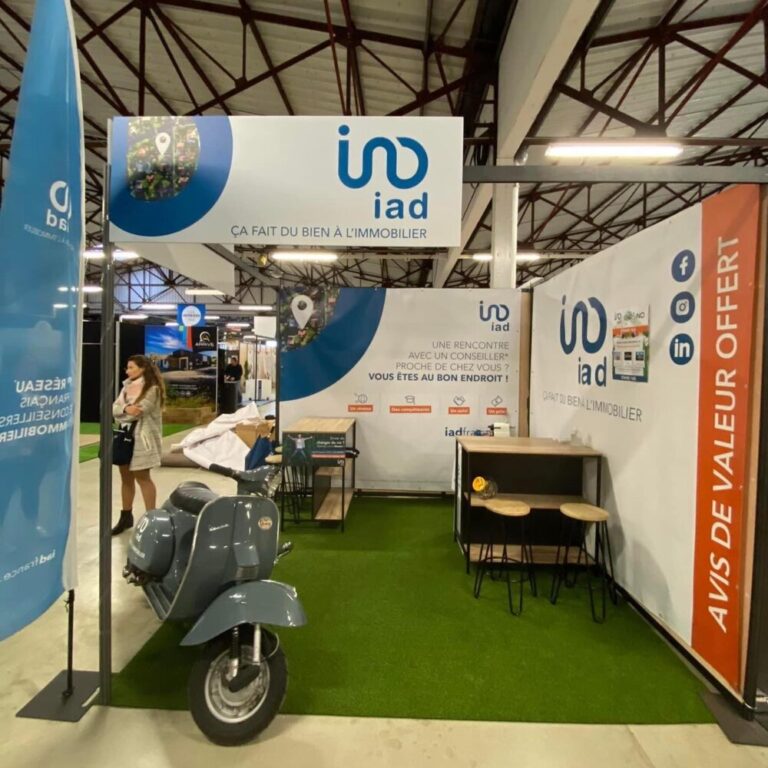 Visuel d'un stand d'exposition pour iad France, incluant un drapeau vertical, des panneaux publicitaires, des bannières de fond de stand, et un scooter Vespa personnalisé avec des adhésifs aux couleurs de l'entreprise, mettant en avant leurs services immobiliers et leur slogan 'Ça fait du bien à l'immobilier'.