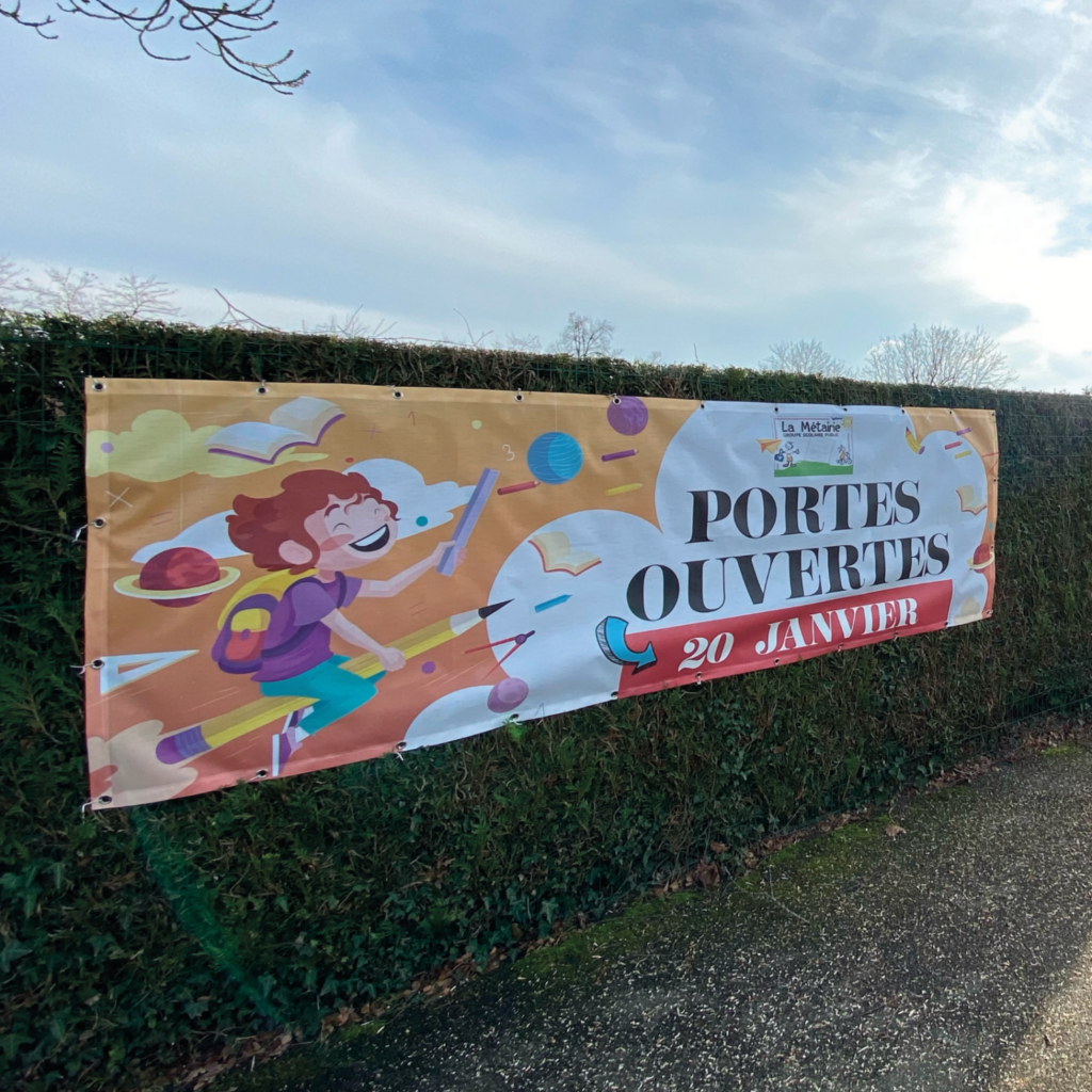 Visuel d'une bannière microperforée pour un événement de portes ouvertes le 20 janvier, illustrée avec un dessin animé d'un enfant joyeux entouré d'objets éducatifs et ludiques, installée le long d'une haie verte.