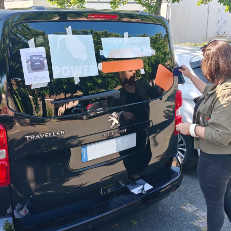 Pauline appliquant des adhésifs publicitaires sur la vitre arrière d'un véhicule utilitaire Peugeot Traveller, avec une autre personne assistant dans le processus.