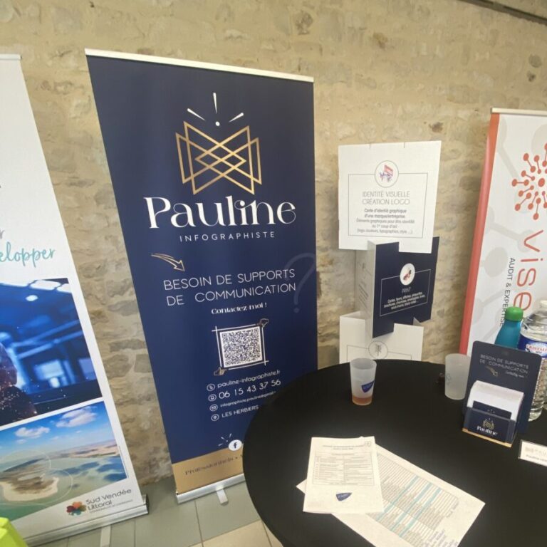 Stand d'exposition avec un roll-up bleu marine présentant le logo et les informations de contact de Pauline Infographiste, spécialisée dans les supports de communication, accompagné d'une tour carrée affichant des informations sur l'identité visuelle et la création de logos.