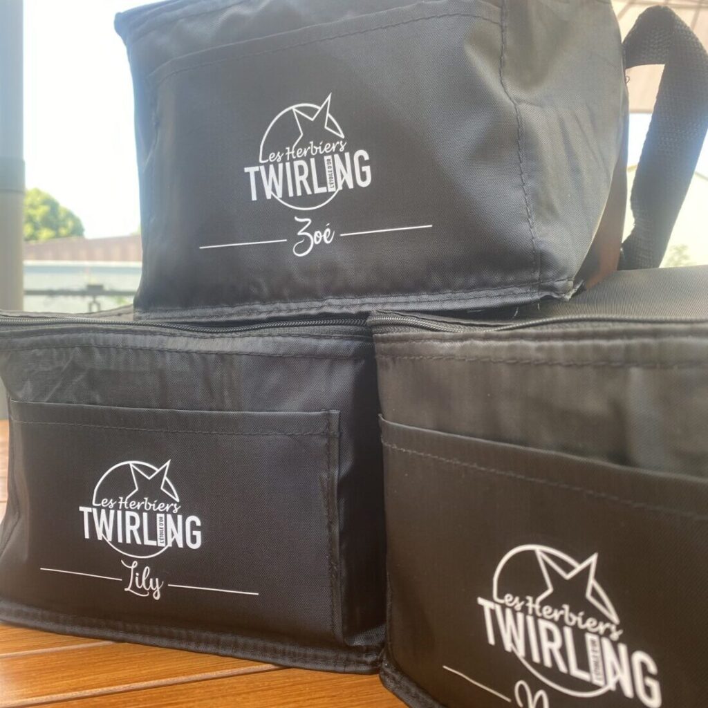 Sacs isothermes personnalisés avec le logo 'Les Herbers Twirling' et des noms individuels tels que Zoé et Lily, parfaits pour des événements ou des activités sportives.