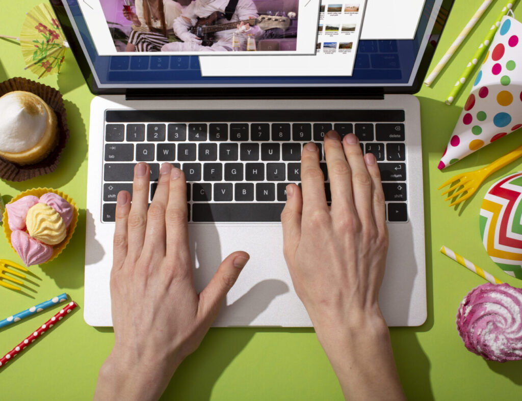 Une personne utilisant un ordinateur portable pour créer des supports de communication événementiels, entourée de divers éléments festifs tels que des cupcakes, des bonbons, des pailles colorées et des chapeaux de fête, illustrant la préparation et la gestion d'événements.